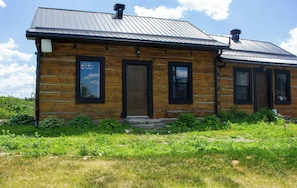 A log cabin with a metal roof, wooden walls, and a front door. - The Lodge | Historic Log Cabin + Hot Tub + Beach Access (Tweed)