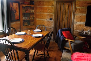 A wooden dining table with chairs, a bookshelf, a television, and a cozy seating area with a red pillow. - The Lodge | Historic Log Cabin + Hot Tub + Beach Access (Tweed)