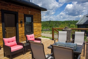 A wooden cabin with a deck, furnished with wicker chairs and a glass-top table. - The Lodge | Historic Log Cabin + Hot Tub + Beach Access (Tweed)
