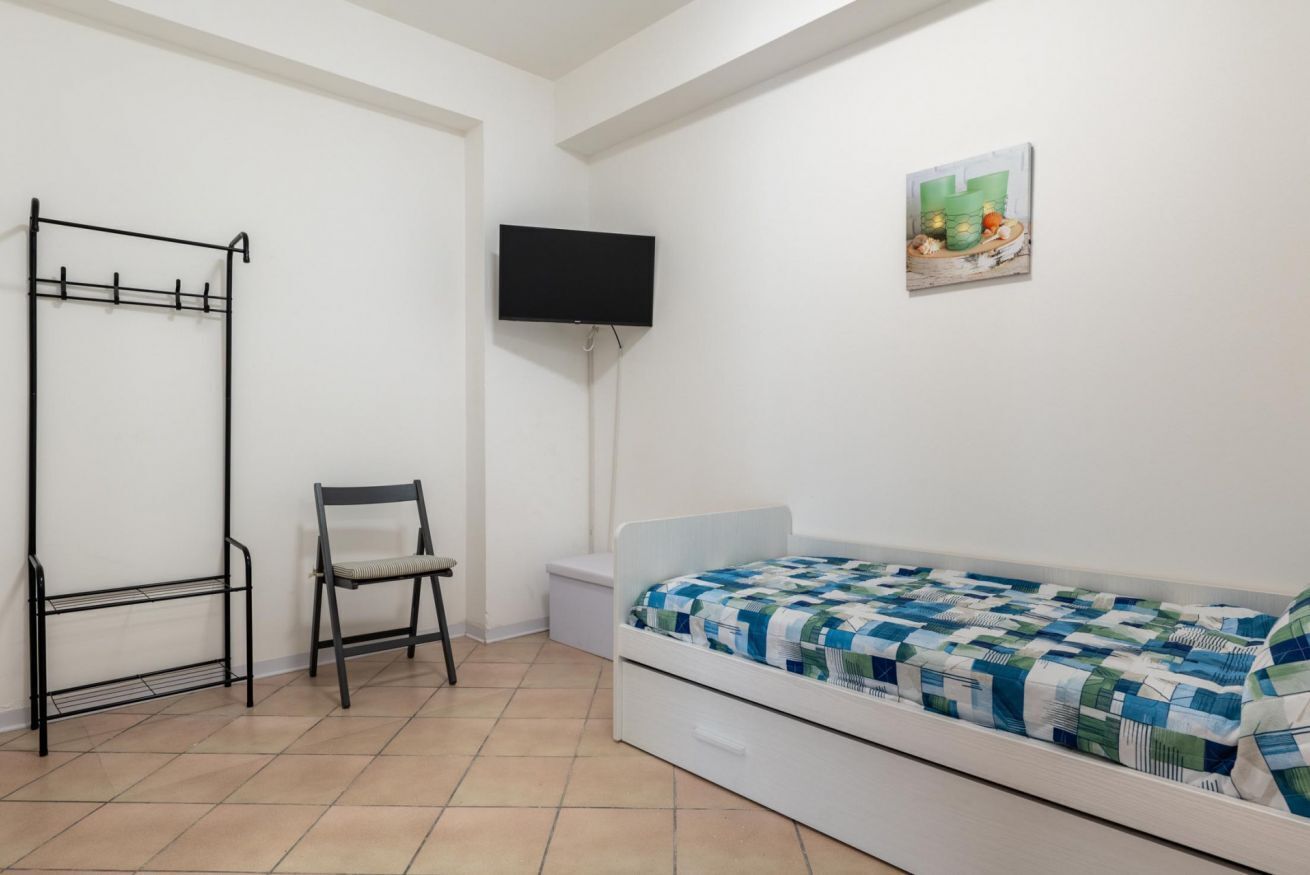 A room with a bed, a chair, a TV, and a wall-mounted shelf.