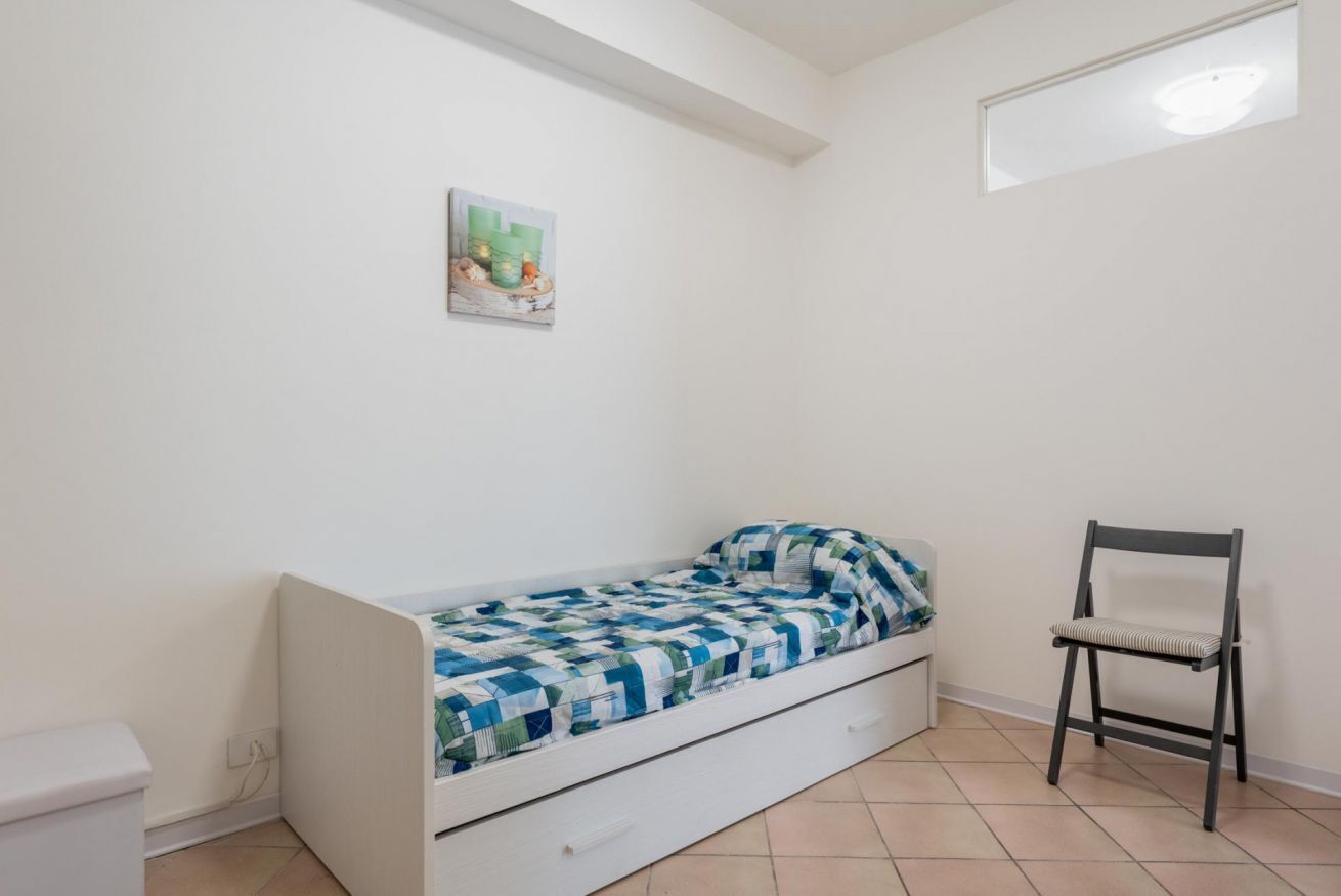 Una habitación pequeña con cama individual, una cama blanca, una silla y un cuadro en la pared.