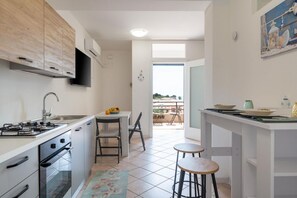 A modern kitchen with a gas stove, oven, and a dining area with a table and chairs. - GuestHost - BaiAmare - Apartment with Shared Pool (Capo Mulini)