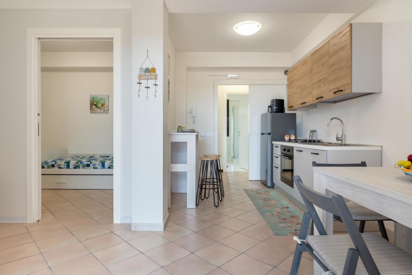 Una cocina compacta con comedor, un taburete pequeño y un refrigerador visible.