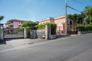 A gated residential area with a paved road, a utility pole, and a building with a pink facade. - GuestHost - BaiAmare - Apartment with Shared Pool (Capo Mulini)