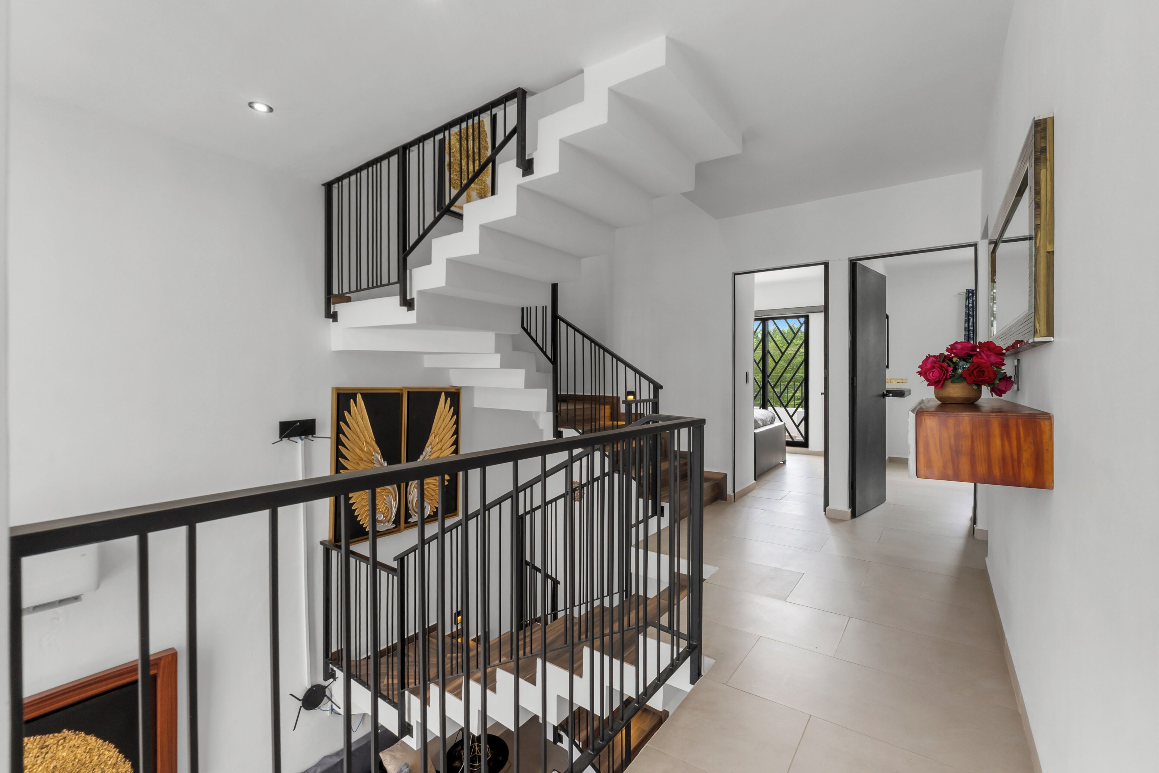 Una escalera moderna con barandal negro, paredes blancas y suelo de madera.