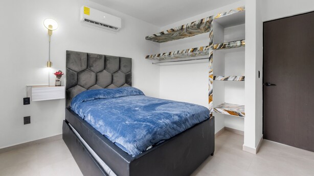 Un dormitorio con cama, aire acondicionado de pared, lámpara de noche y una puerta.