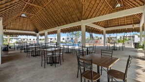 Un área de comedor al aire libre con techos de paja, mesas y sillas.