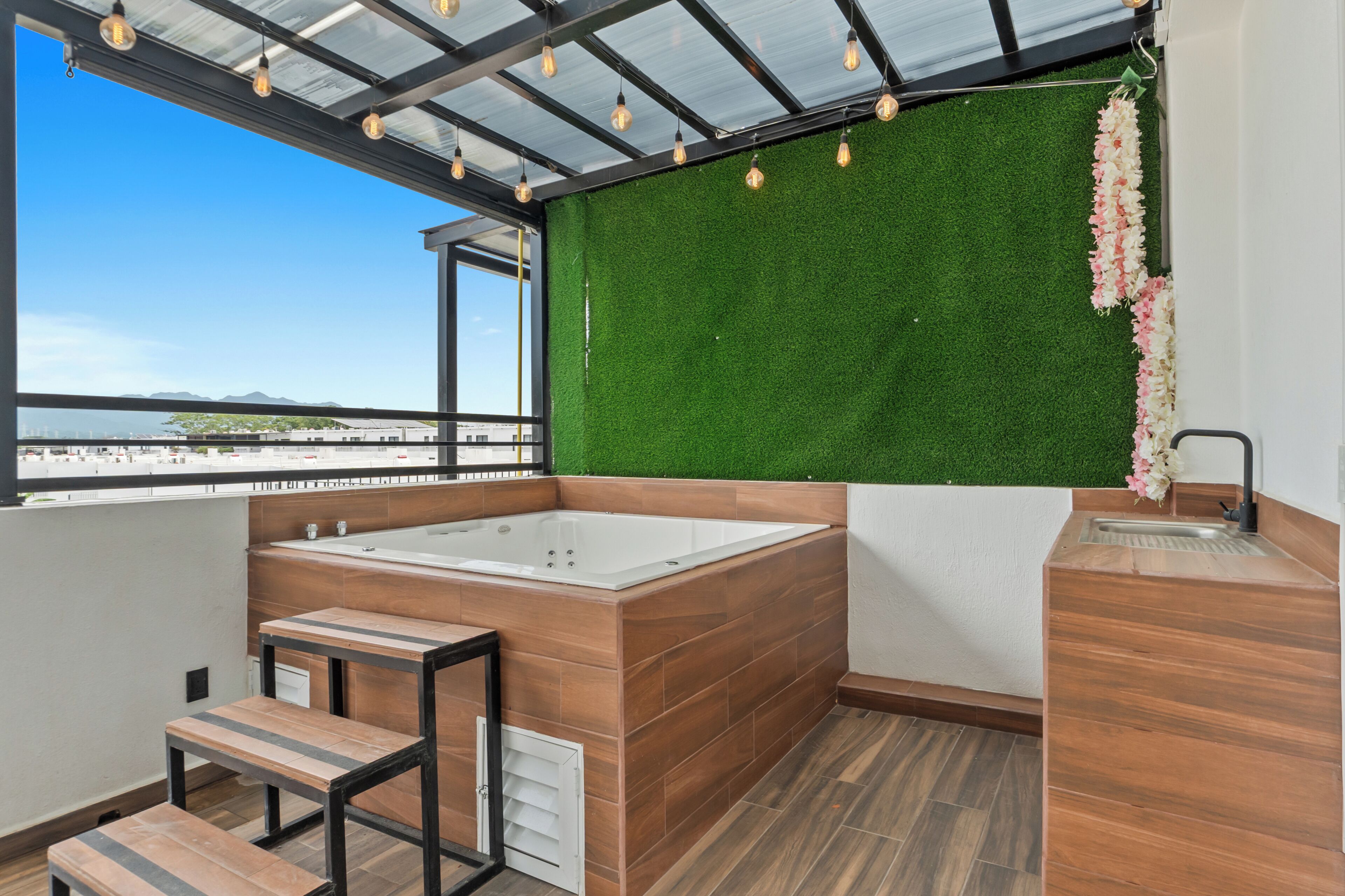 A modern bathroom with a large bathtub, wooden flooring, and a green artificial grass wall.