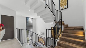 Una escalera moderna con barandilla de metal negro, paredes blancas y peldaños de madera.