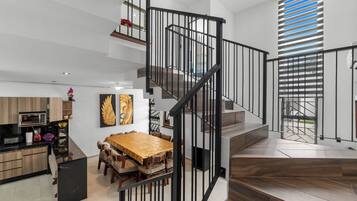 A modern interior with a wooden dining table, a staircase with black railings, and a kitchen area.