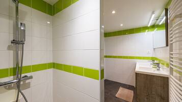 Een badkamer met witte en groene tegels, een douche, een wastafel met spiegel en een houten kastje.