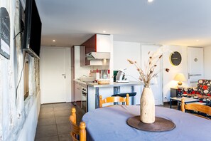A modern kitchen with a built-in oven, a dining area with a round table, and a living room with a sofa and a wall clock.