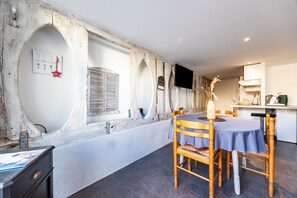 A dining area with a wooden table and chairs, a white wall with a decorative plaque, and a kitchen area in the background.