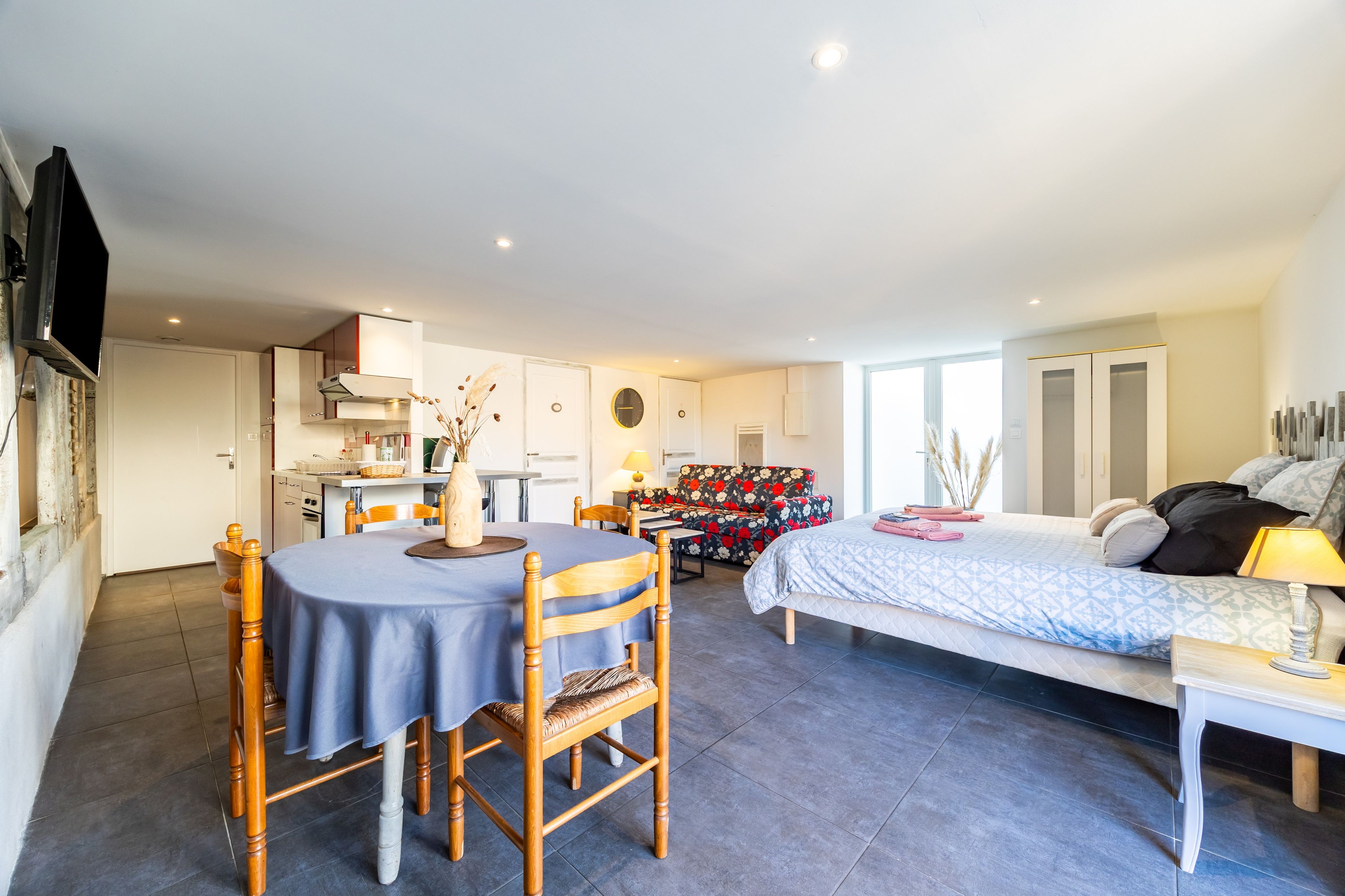 A modern interior with a dining area, kitchen, and a bedroom with a bed and bedside table.