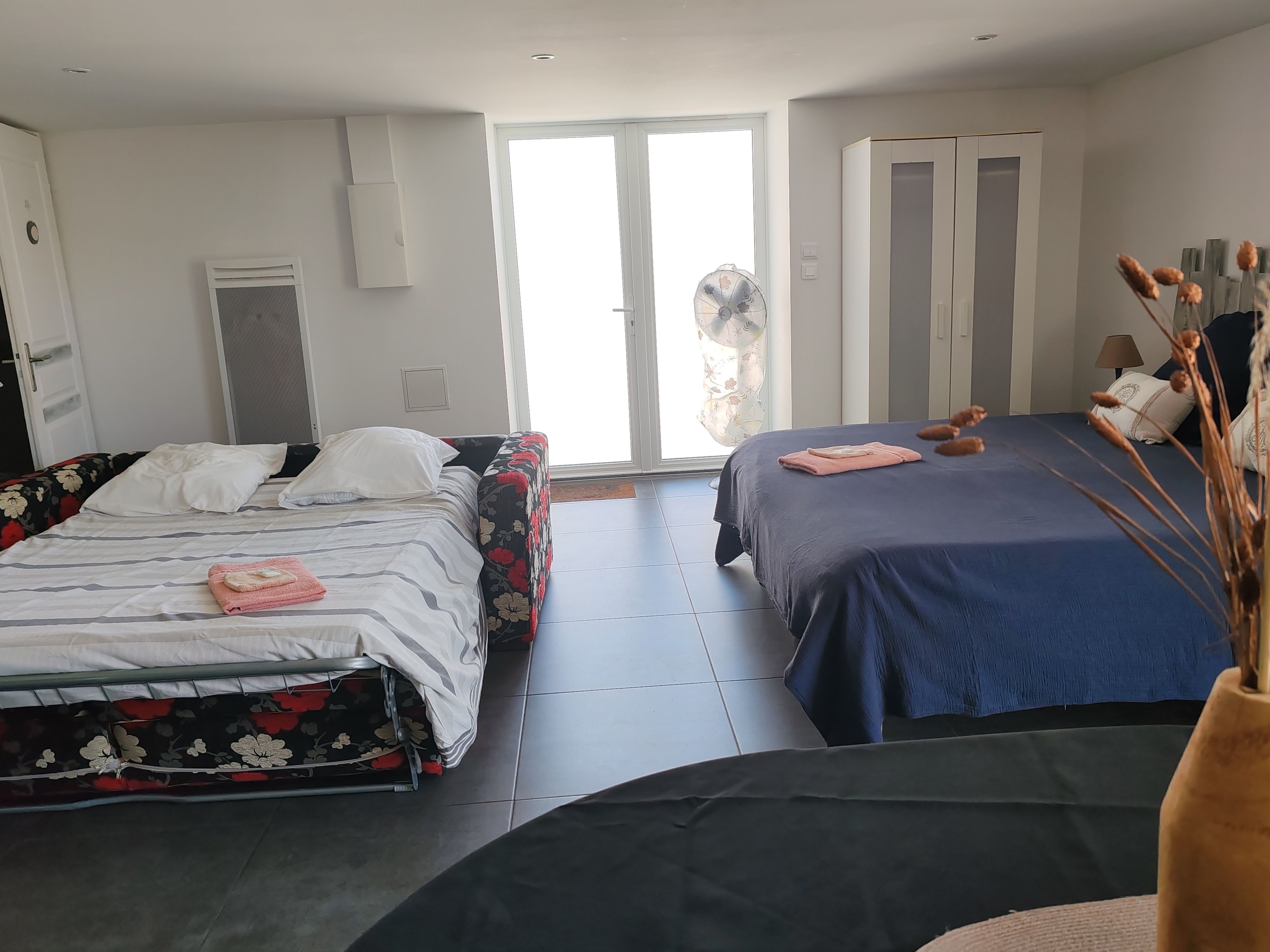 Et hotelværelse med to senge, et stort vindue, en ventilator og et klædeskab.