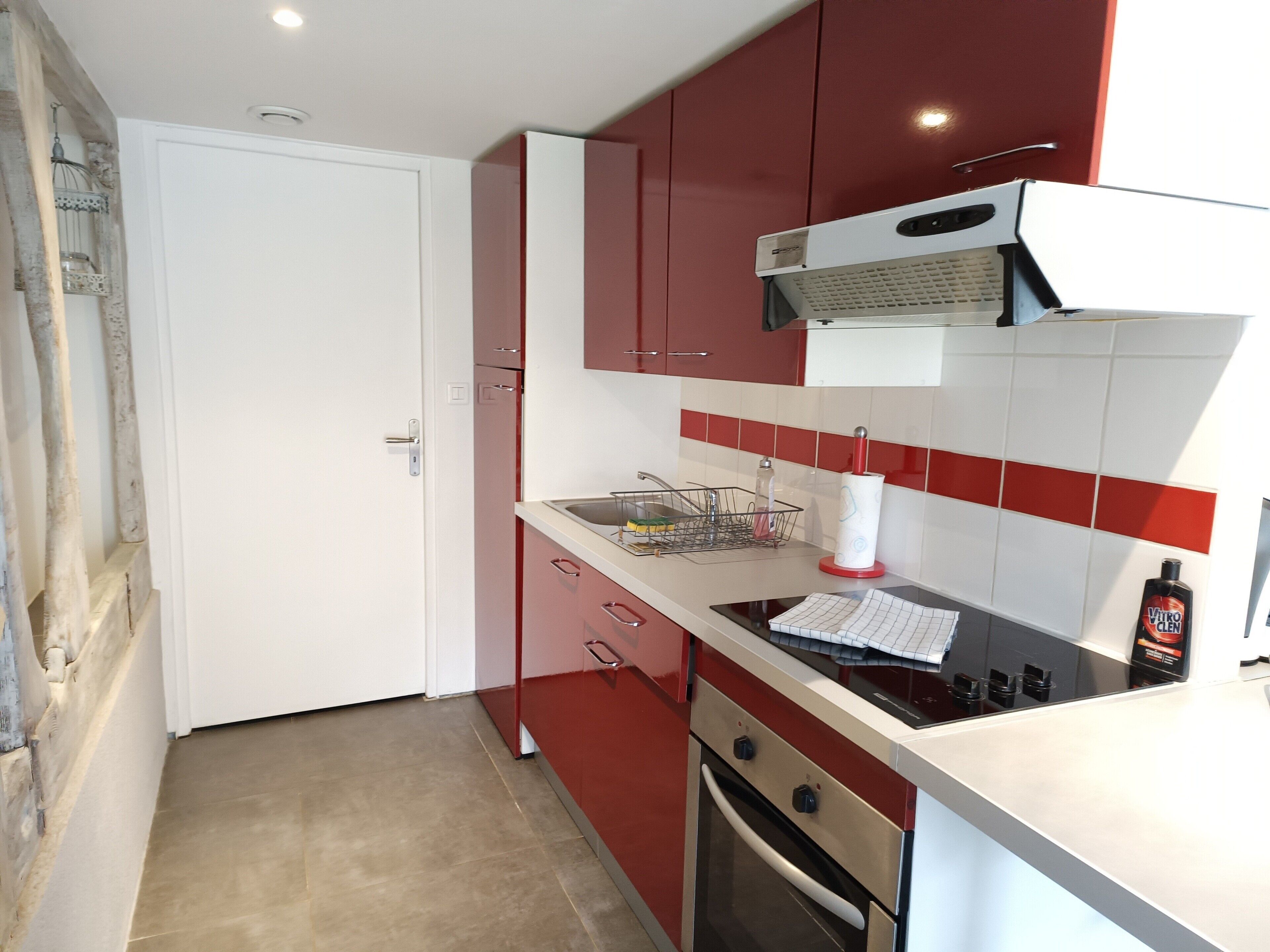 Une cuisine avec des meubles de rangement rouges, un plan de travail blanc, une cuisinière et un évier.