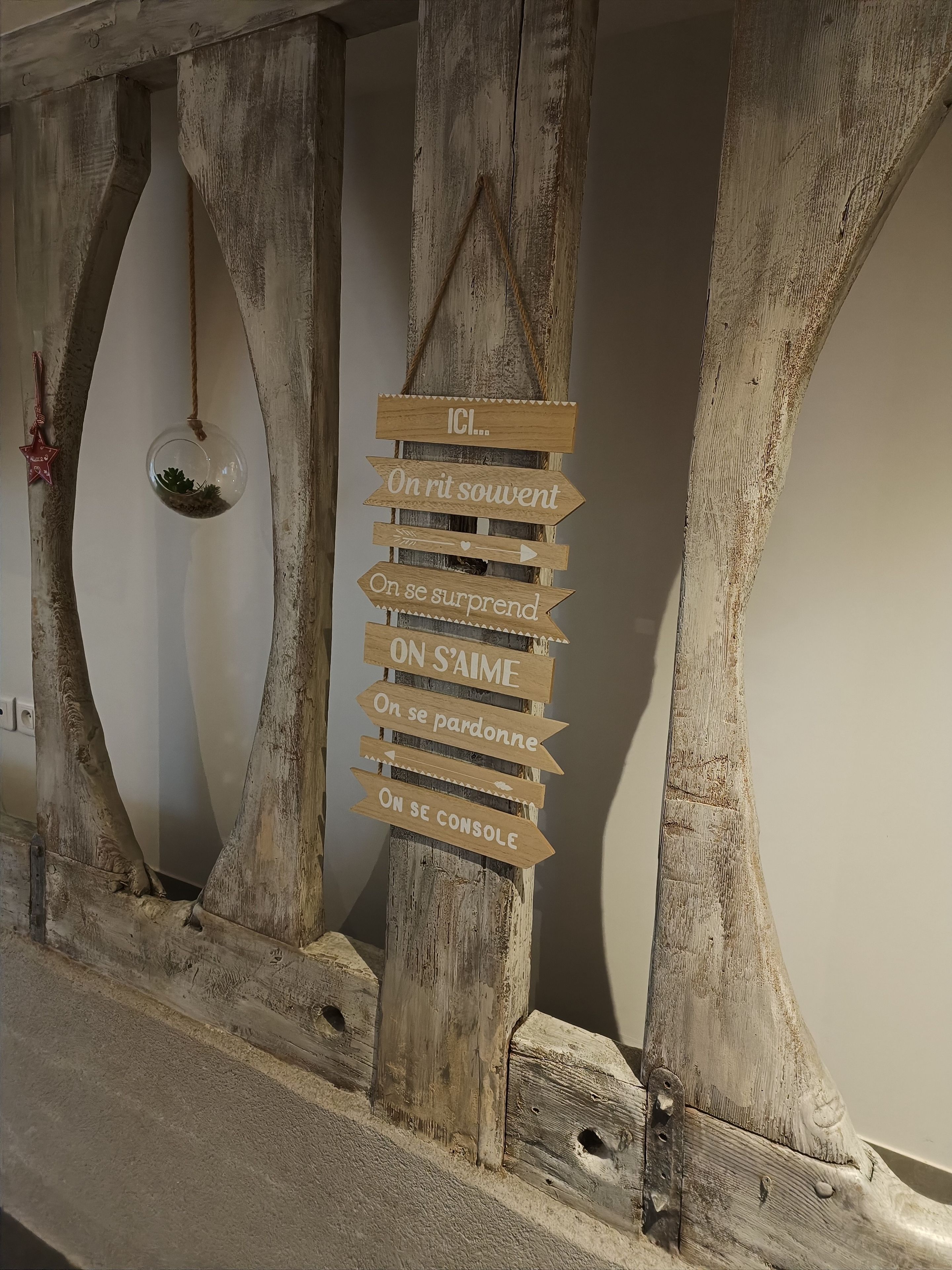 Un panneau en bois rustique, orné de flèches indiquant les directions et d’un texte, fixé sur une structure en bois usée par les intempéries.