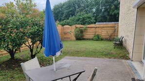 Un patio al aire libre con mesa y sillas, una sombrilla azul y una valla de madera al fondo.