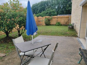 Une terrasse extérieure avec une table et des chaises, un parasol bleu et une clôture en bois en arrière-plan.
