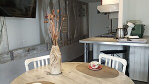 Un comedor con una mesa redonda, dos sillas, un florero con flores secas y un televisor montado en la pared.