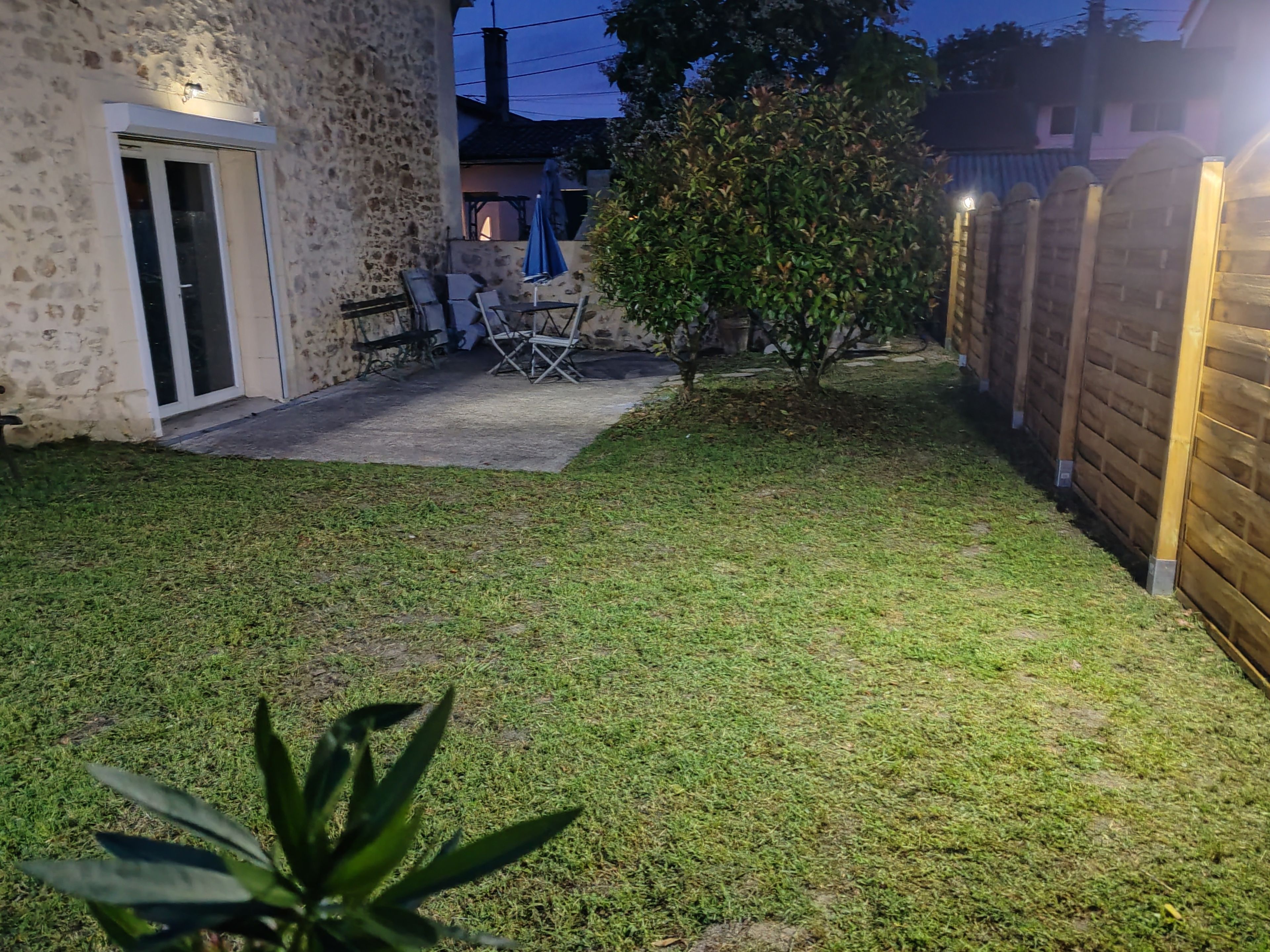 A backyard with a patio area, a wooden fence, and a small tree.