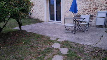 Un espace patio aménagé avec une table et des chaises, un parasol bleu et un chemin de pierre menant à un bâtiment à la façade en pierre.