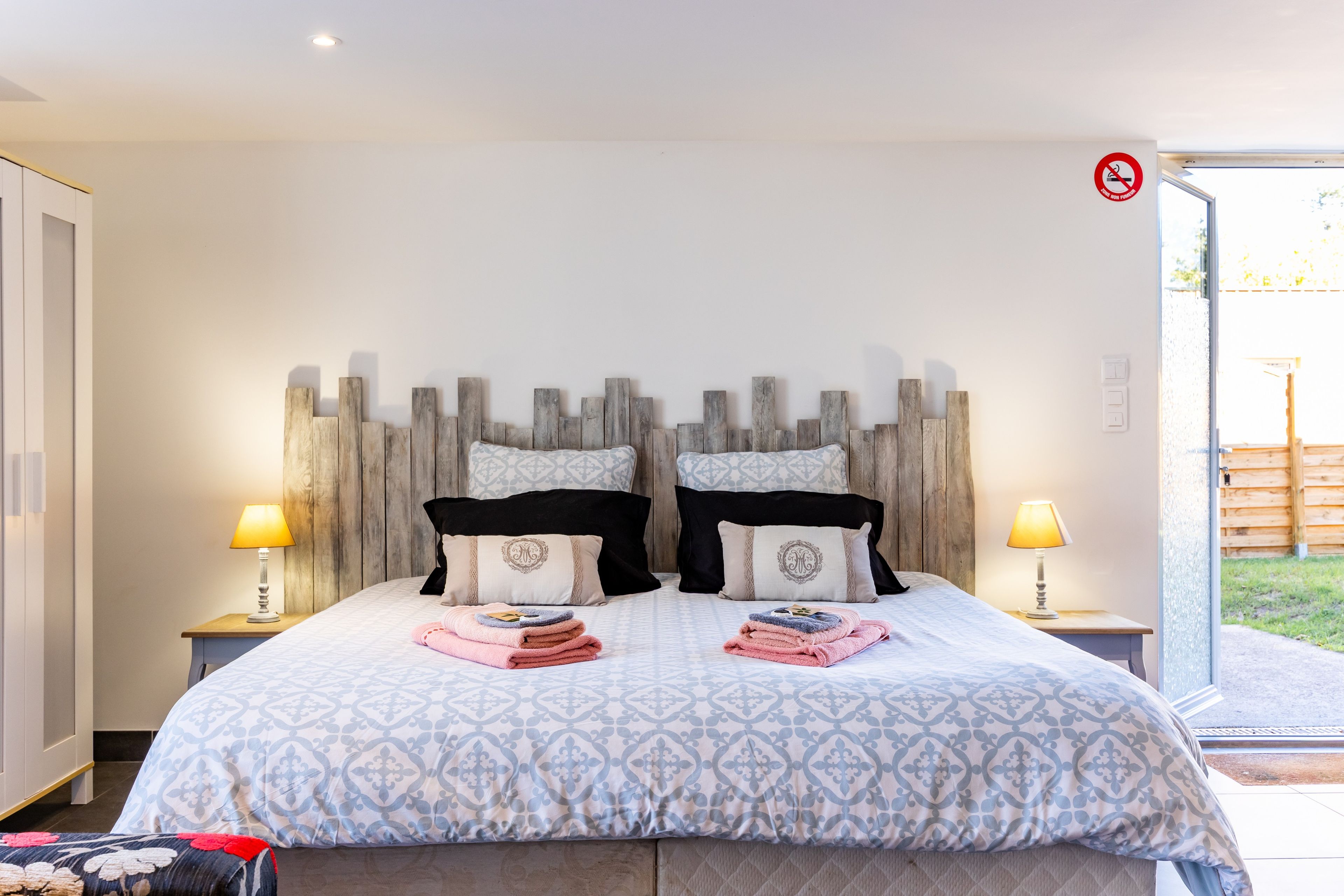Ein Hotelzimmer mit Bett, zwei Nachttischlampen, einem Holzkopfschild und Blick ins Freie.