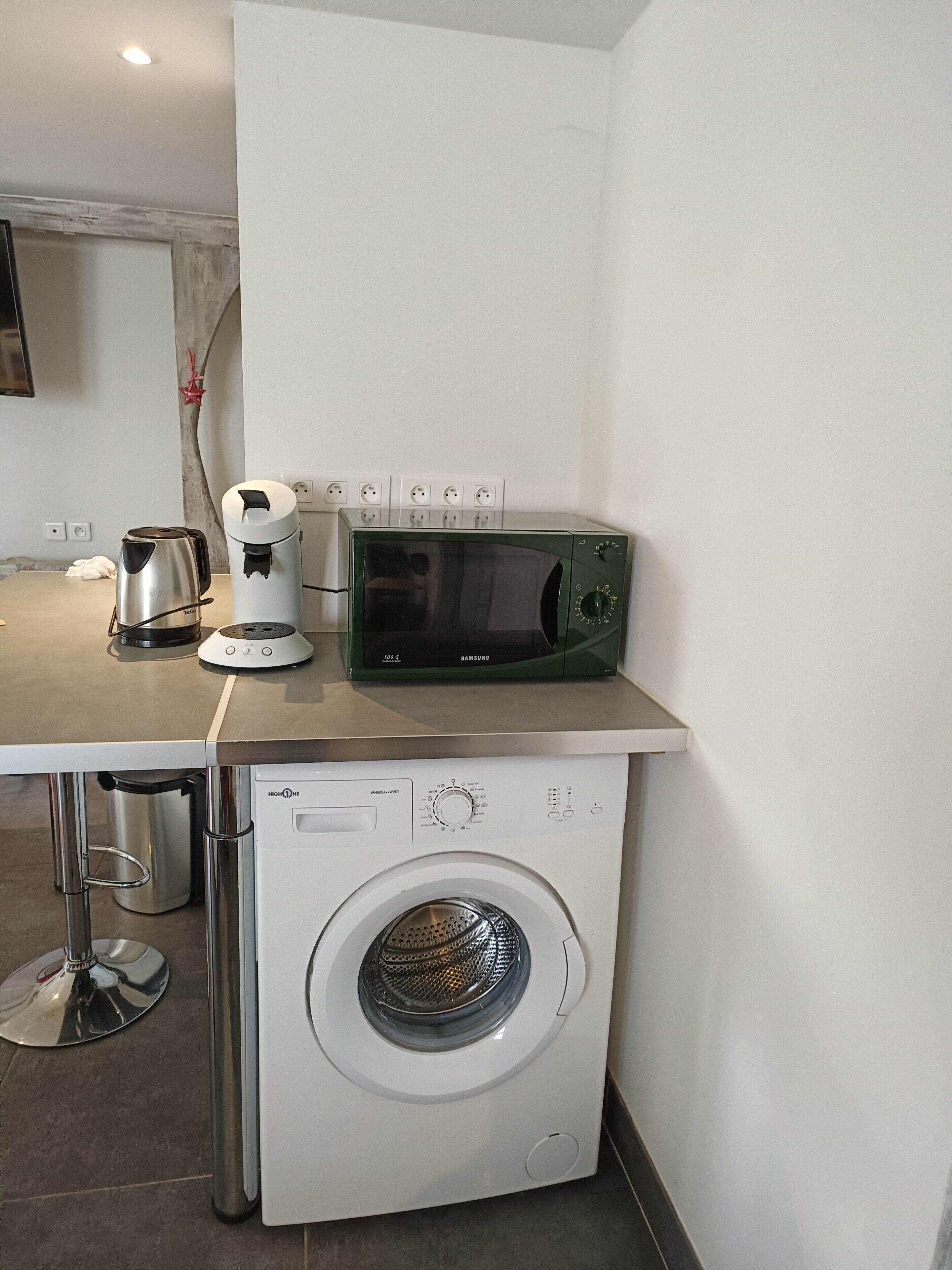 Une petite cuisine équipée d’un four à micro-ondes, d’une machine à café et d’un lave-linge.