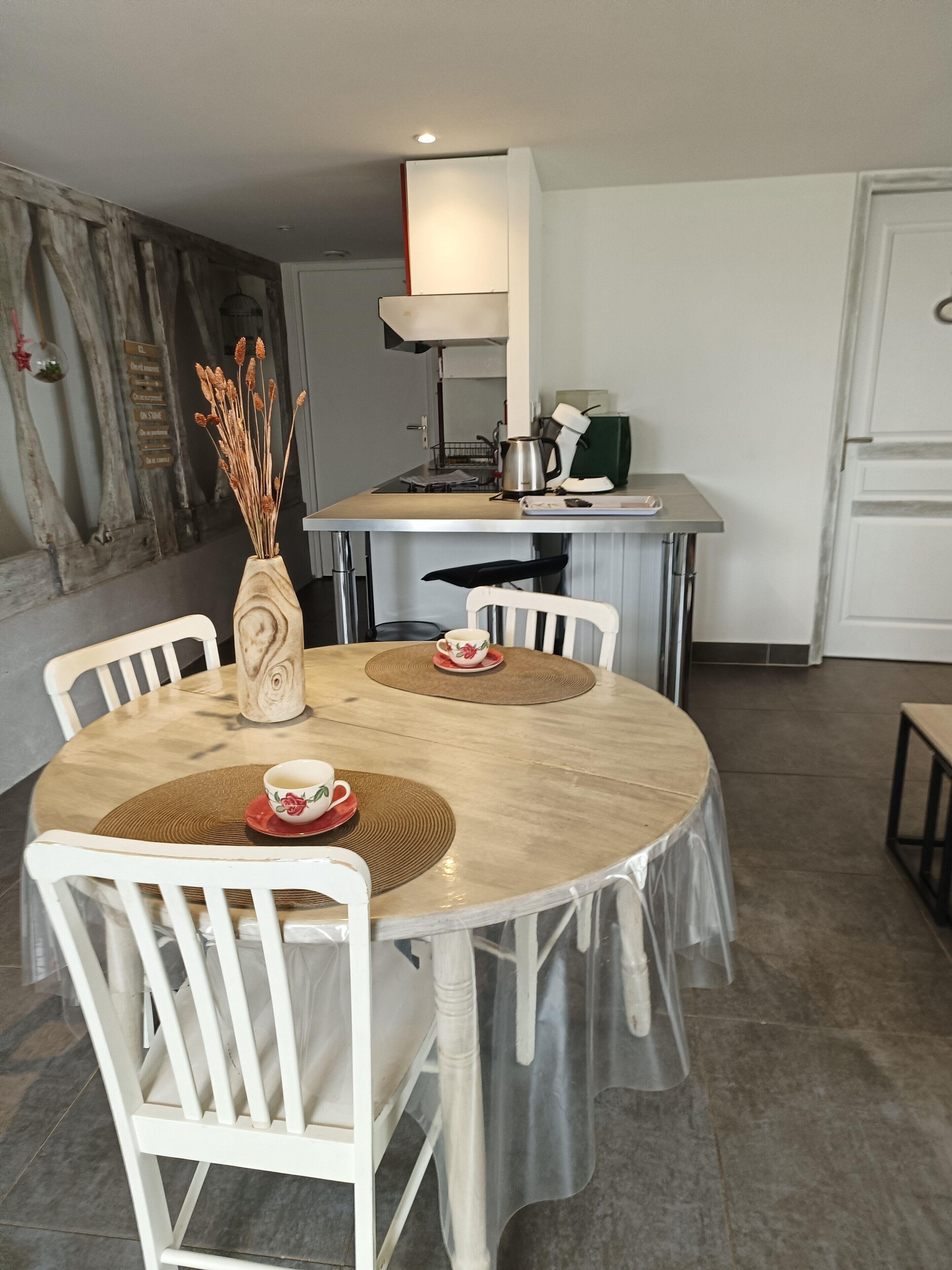 Un coin repas avec une table ronde, des chaises blanches et un vase contenant des plantes séchées.