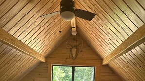 Une cabane avec deux lits, un ventilateur de plafond et une fenêtre donnant sur la forêt.