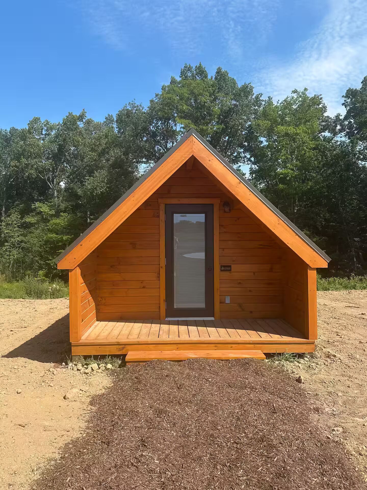 A wooden cabin with a pitched roof, a door, and a small porch area.