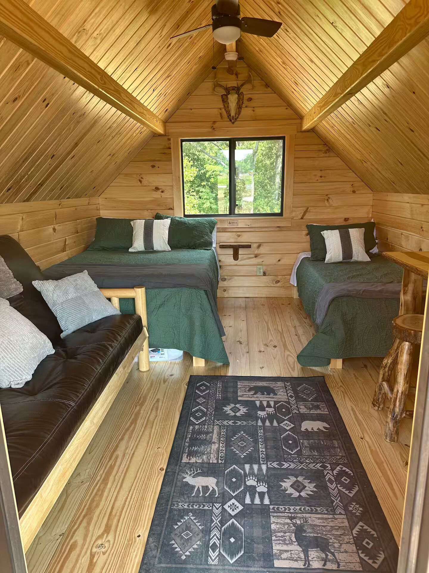 A cozy attic bedroom with two beds, a wooden ceiling, and a large window.