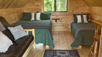 A cozy attic bedroom with two beds, a wooden ceiling, and a large window.
