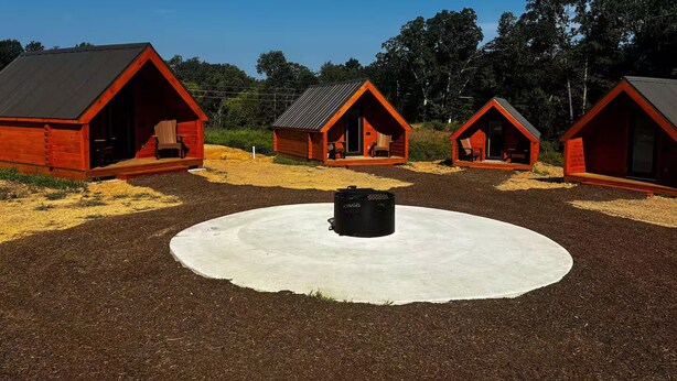 Une rangée de cabanes en bois rouges, avec une zone centrale circulaire en béton.