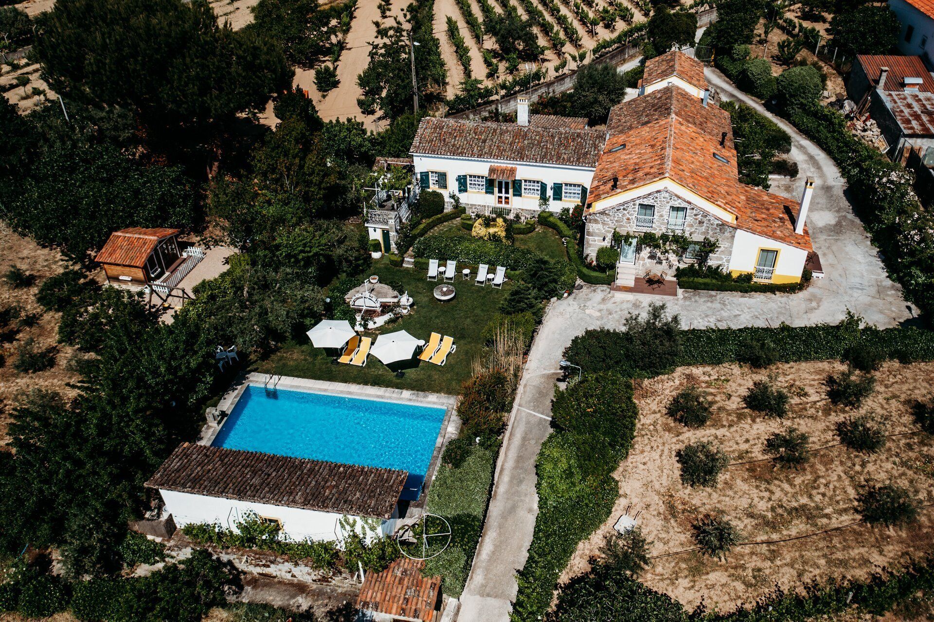 An aerial view of a property with a swimming pool, a large house with a tiled roof, and a well-maintained garden.