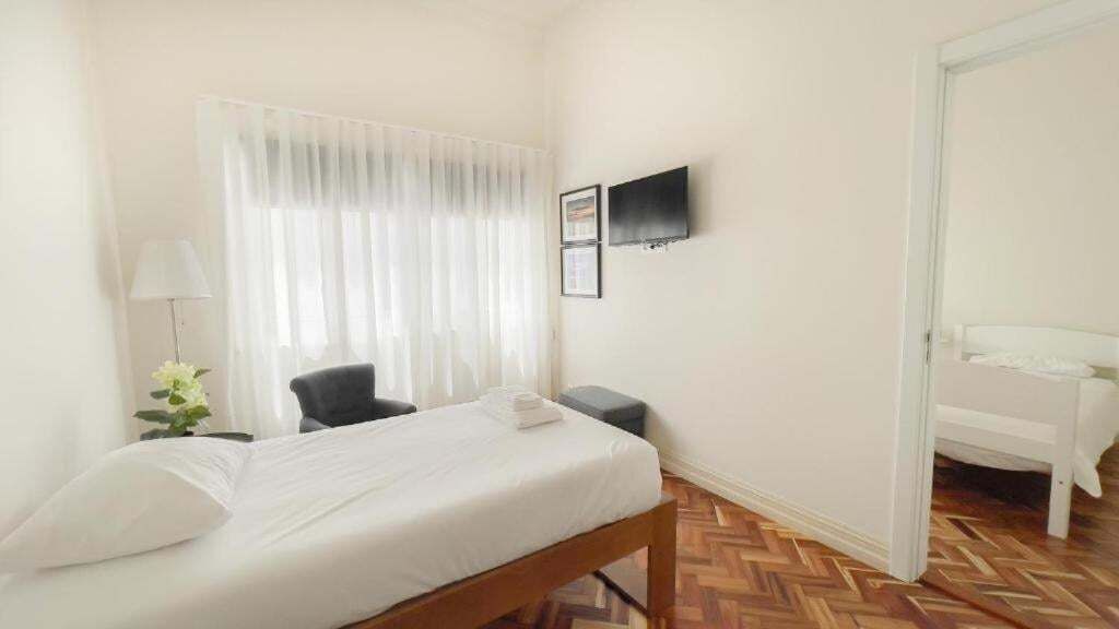Une chambre d’hôtel avec un lit, une chaise, une petite table, un téléviseur fixé au mur et un parquet en bois disposé en motif à chevrons.