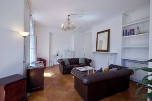 Ein Wohnzimmer mit einer Chandelier, Ledersofas, einem Couchtisch und einem Bücherregal mit Büchern.