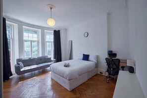 Ein Schlafzimmer mit Bett, Schreibtisch, Sessel, Sofa und Fenster.