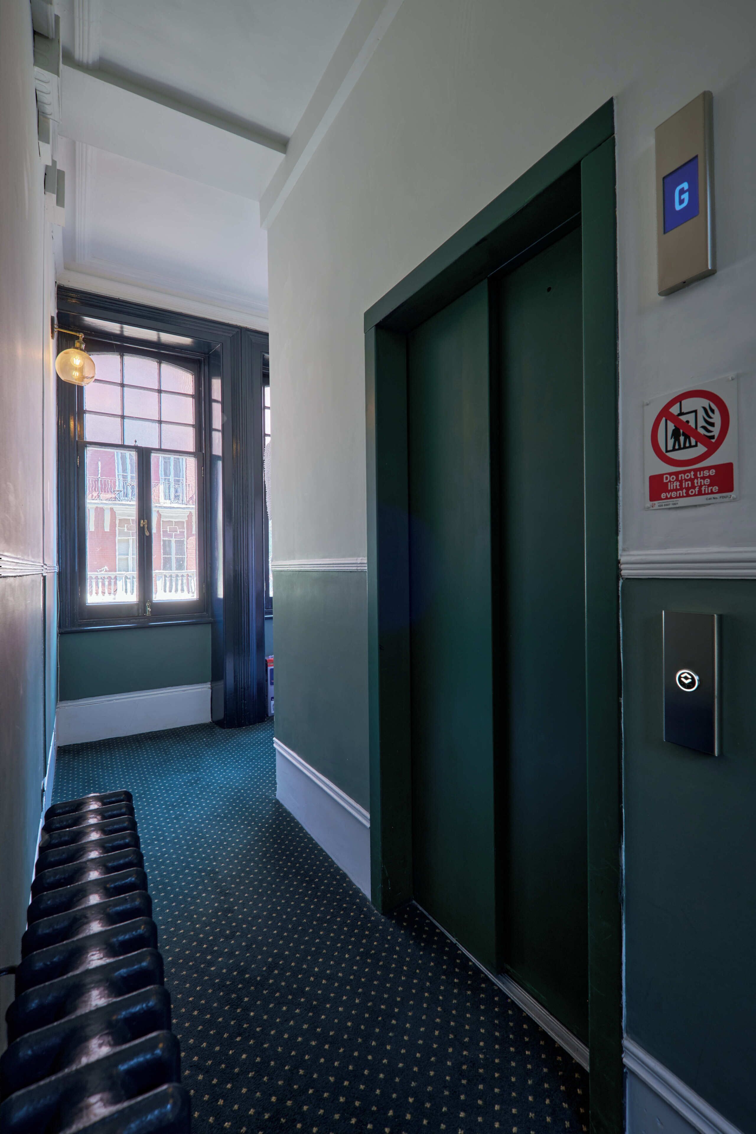 A narrow hallway with a patterned floor, a door with a lift sign, and a no-lift-in-fire event sign.