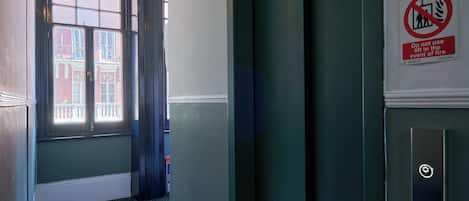 A narrow hallway with a patterned floor, a door with a lift sign, and a no-lift-in-fire event sign.