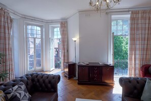 A spacious living room with a large window, a dark wooden cabinet, and a leather sofa. - A Grand Victorian Mansion Apartment in Marylebone (London)