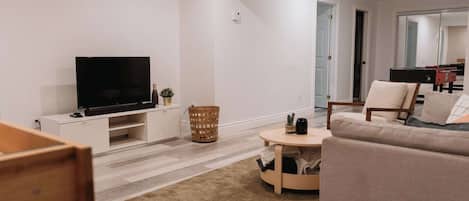 A modern living room with a flat-screen TV, a sofa, a small round table, and a wooden cabinet.
