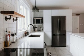 Eine moderne Küche mit weißen Schränken, einem Edelstahl-Kühlschrank, einer Mikrowelle und einer Kochinsel mit Glasplatte und Spüle.