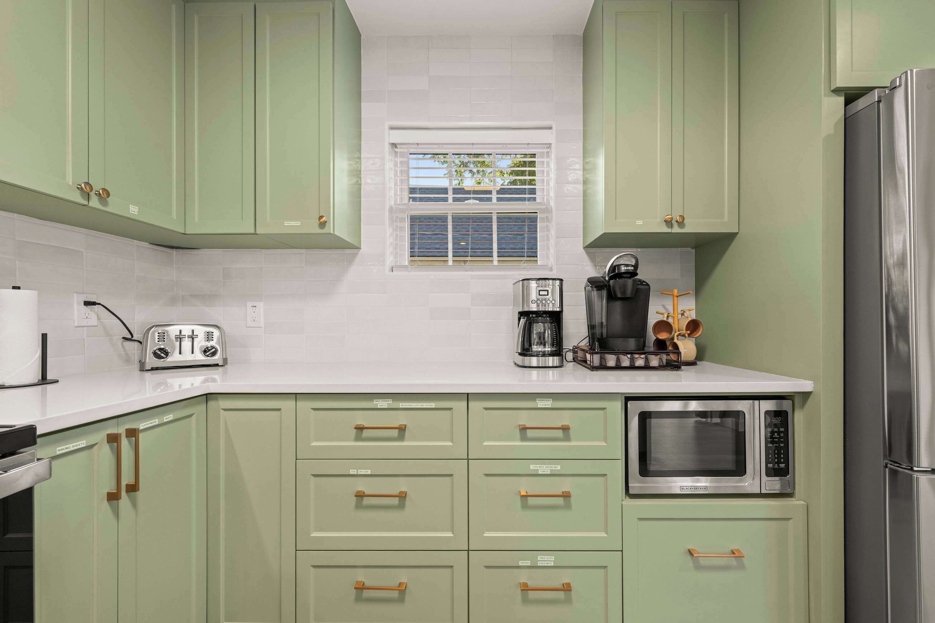 A kitchen with green cabinets, a white countertop, a toaster, a coffee maker, and a microwave.