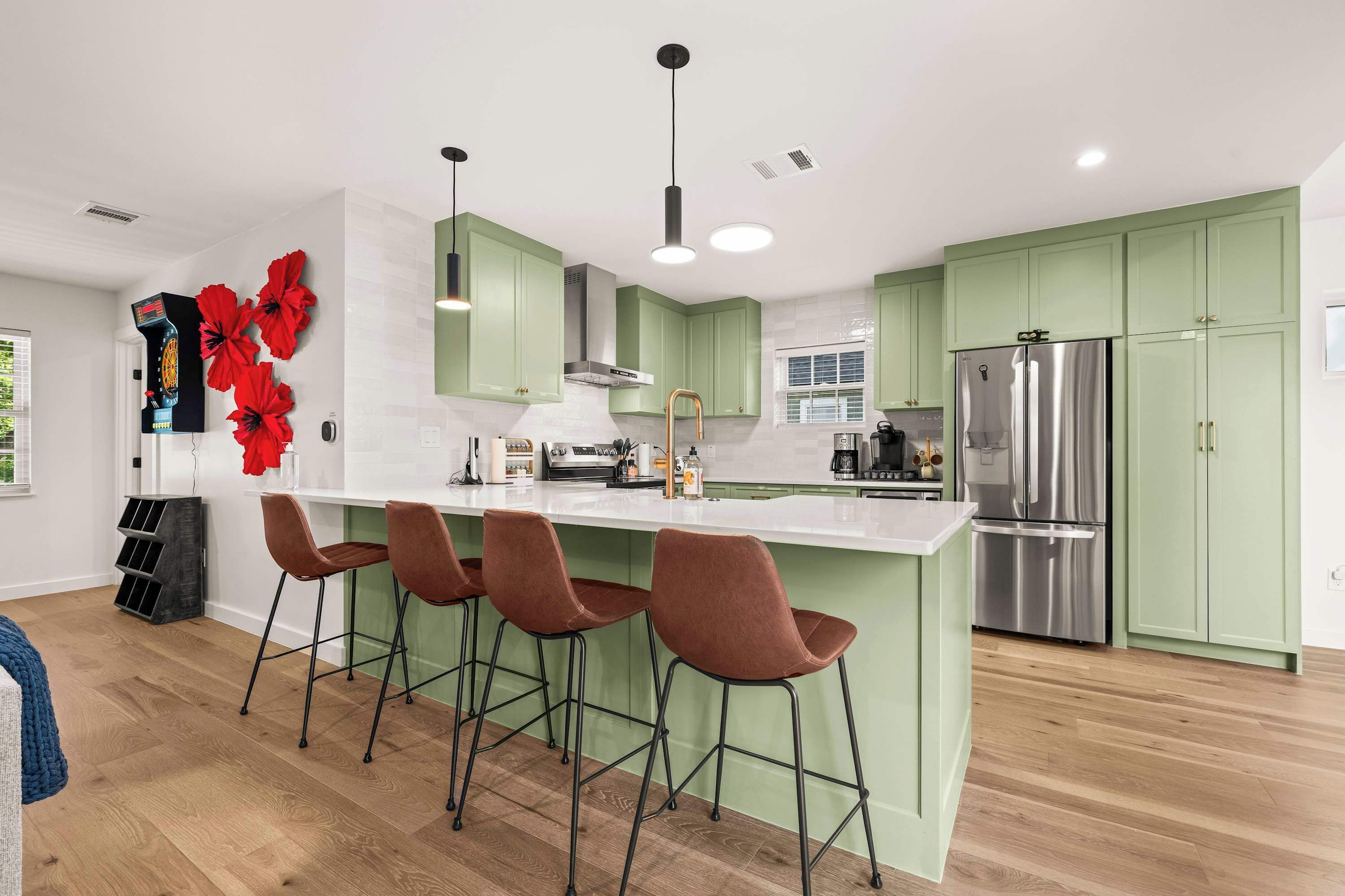 A modern kitchen with green cabinets, a stainless steel refrigerator, and a bar area with stools.