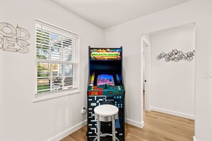 A room with a retro arcade machine, a window with blinds, and a wall with a bicycle decoration. - Cozy Chic House Pet-Friendly  Sleeps 12 (Georgetown)