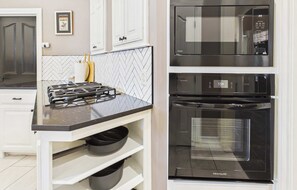 Een keuken met een gasfornuis, een magnetron en een oven. Er zijn witte kasten en een backsplash met een herringbone patroon.