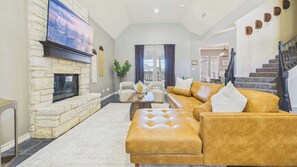 Ein Wohnzimmer mit Kamin aus Stein, einem großen Flachbildfernseher, einem gelben Ledersofa und einer Treppe, die eine weitere Ebene hinaufführt.