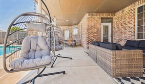 A covered patio with a pool, outdoor seating, and a brick wall.
