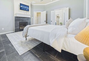 A bedroom with a bed, a fireplace, a television mounted on the wall, and a door leading to another room.